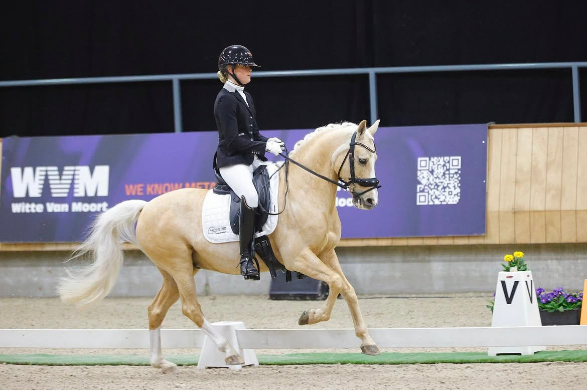 Annabell van der Horst cantering her palomino pony at the Dutch Indoor Championships, wearing a JuulC show jacket