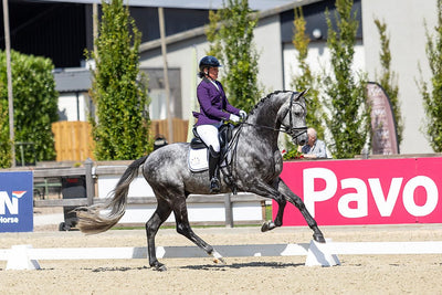 Danielle Heijkoop cantering a dapple grey horse during a dressage test in a JuulC show coat