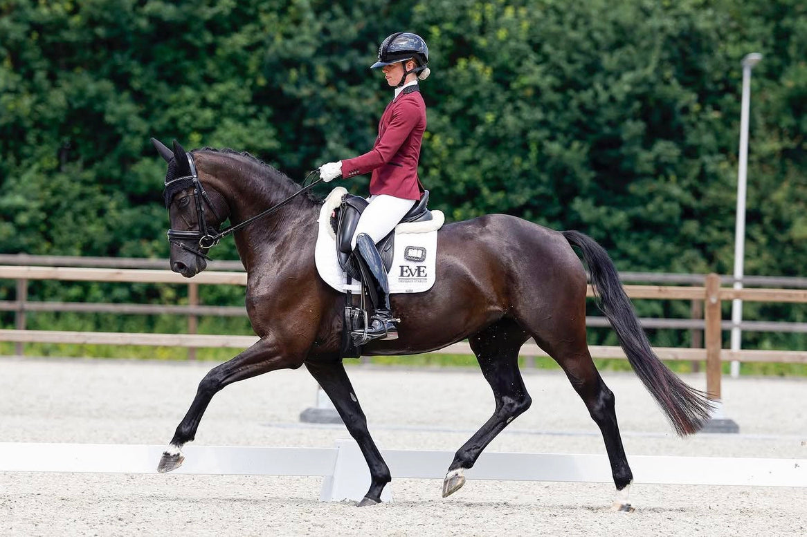Eline van Egmond trotting in an outdoor arena during her competition, in a JuulC show jacket