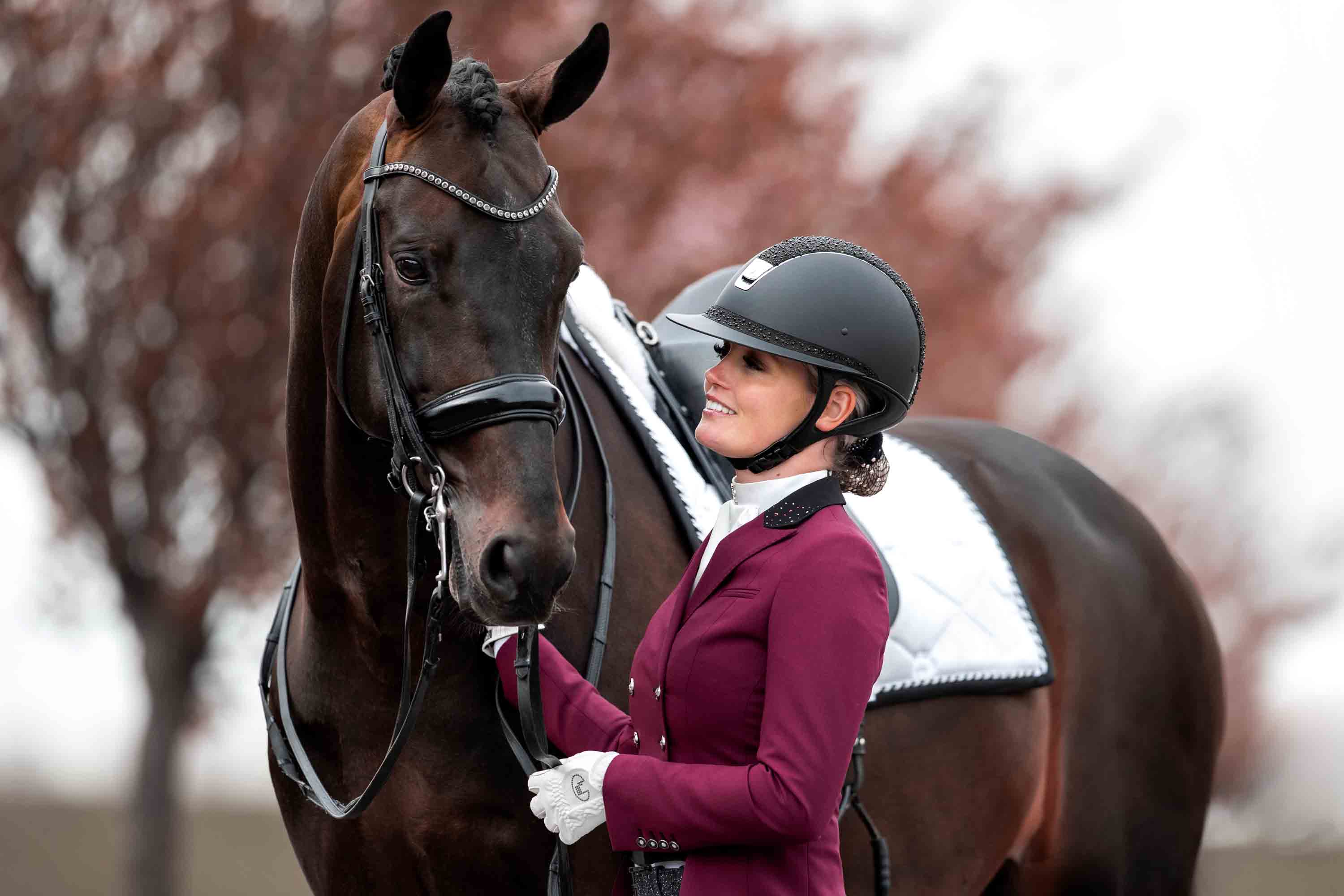 Renate van Uytert smiling while looking at her dark bay stallion, wearing a short frack from JuulC